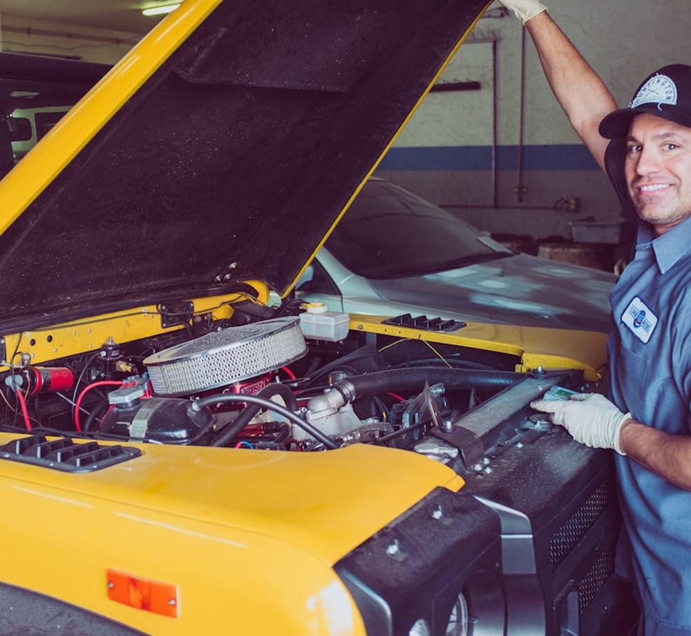 Smiling technician standing beside a car with its hood open